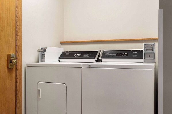 A compact, modern laundry room with a built-in washer and dryer, a wooden shelf above, and a door with a brass handle.