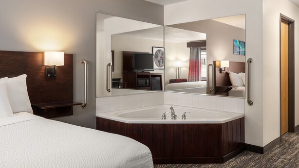 A hotel room with a large bed, a separate bathroom with a bathtub, a large mirror, and a television in the corner.