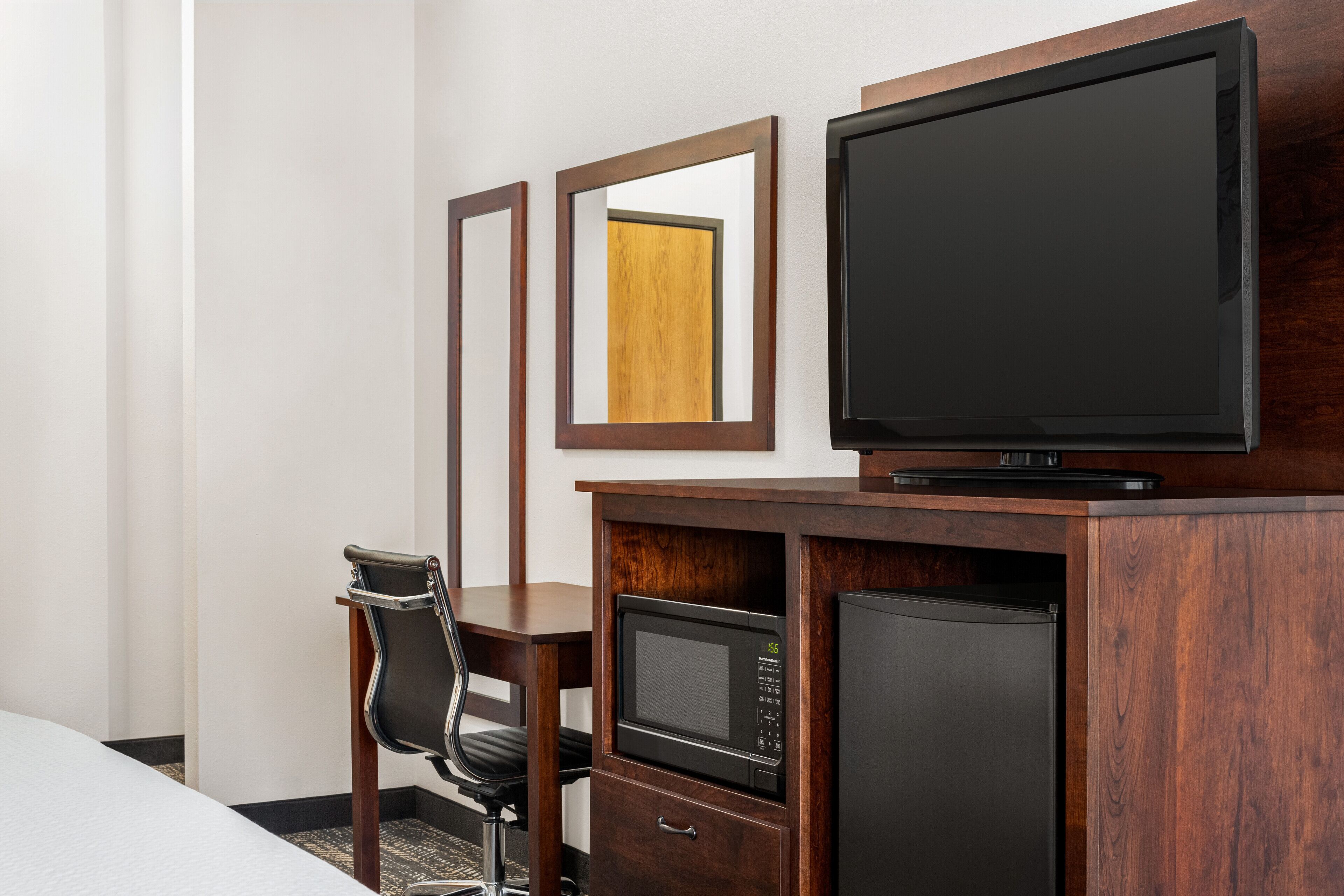 A hotel room with a bed, a desk with a chair, a microwave, a refrigerator, and a television on a wooden cabinet.