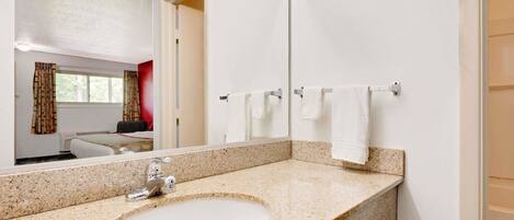 Une salle de bain avec un lavabo doté d’un plan de travail en granit, un grand miroir et un porte-serviettes avec des serviettes blanches.