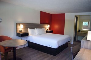A hotel room with a bed, bedside tables, a round table, and a chair. - Ramada by Wyndham Cleveland Airport West (Fairview Park)