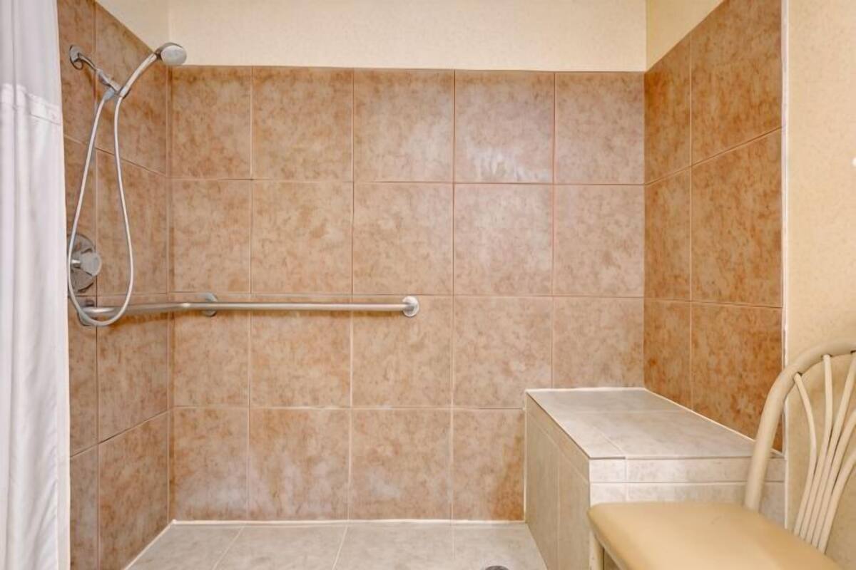 Un baño con ducha, barras de apoyo y un banco.