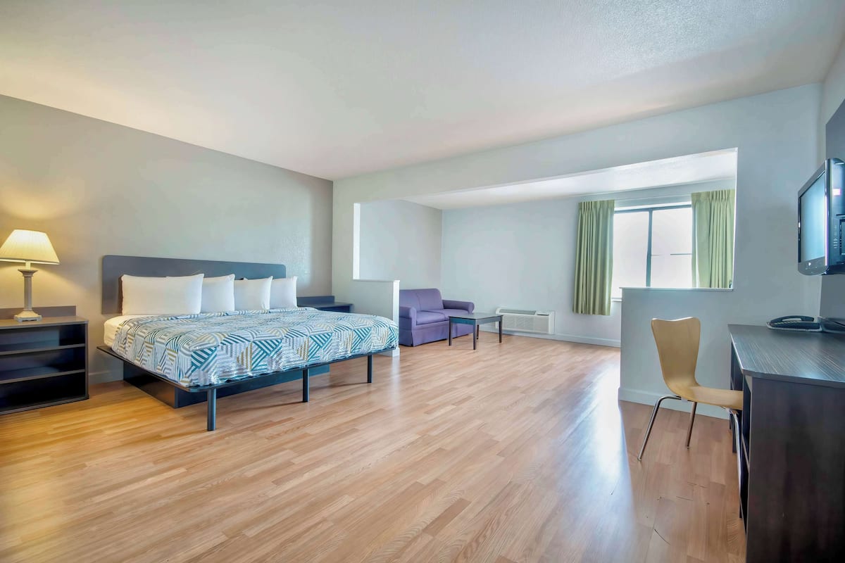 A modern hotel room with a bed, a desk, a chair, and a sofa.
