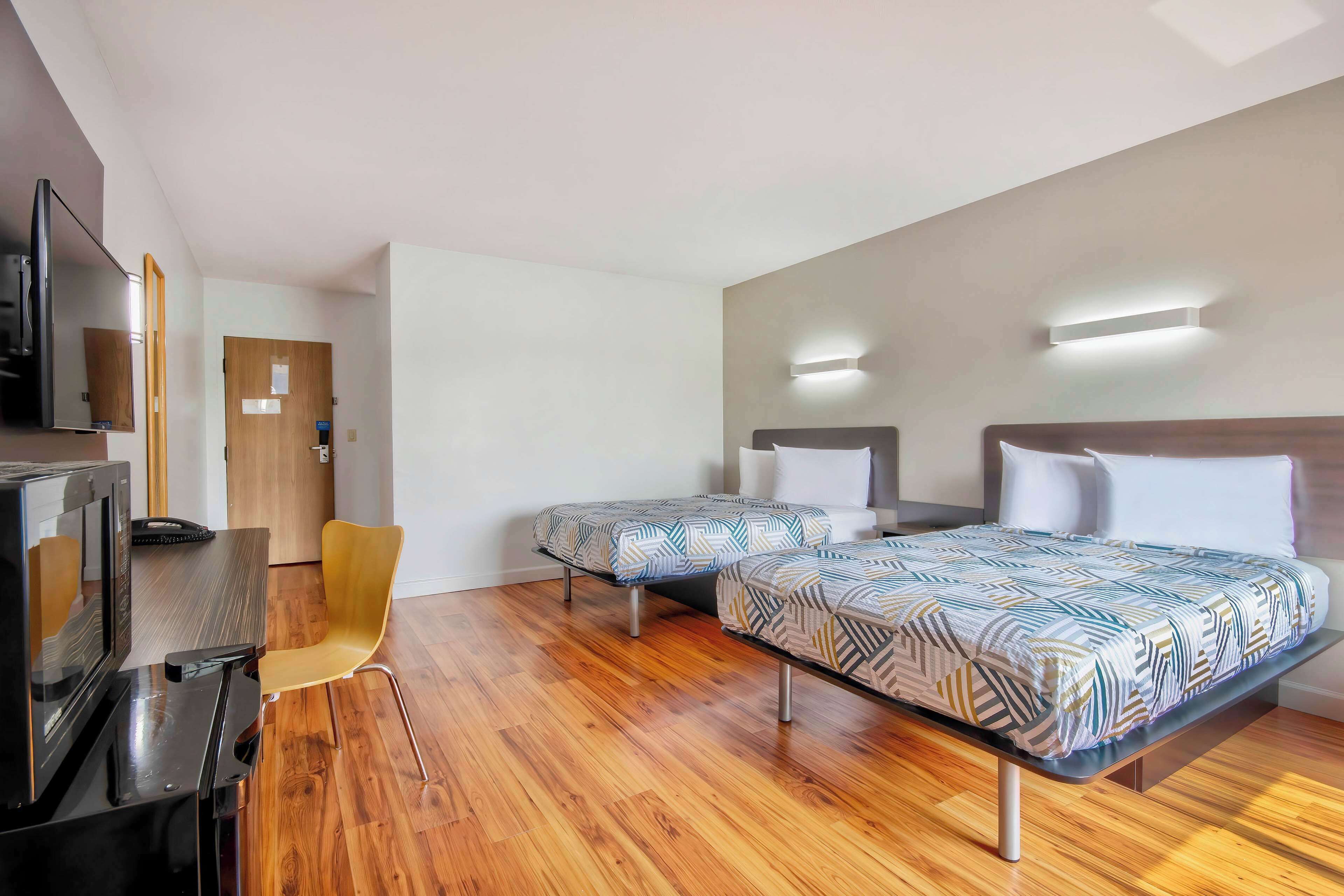 A hotel room with two beds, a desk, a chair, and a TV.