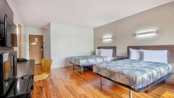 A hotel room with two beds, a desk, a chair, and a TV.