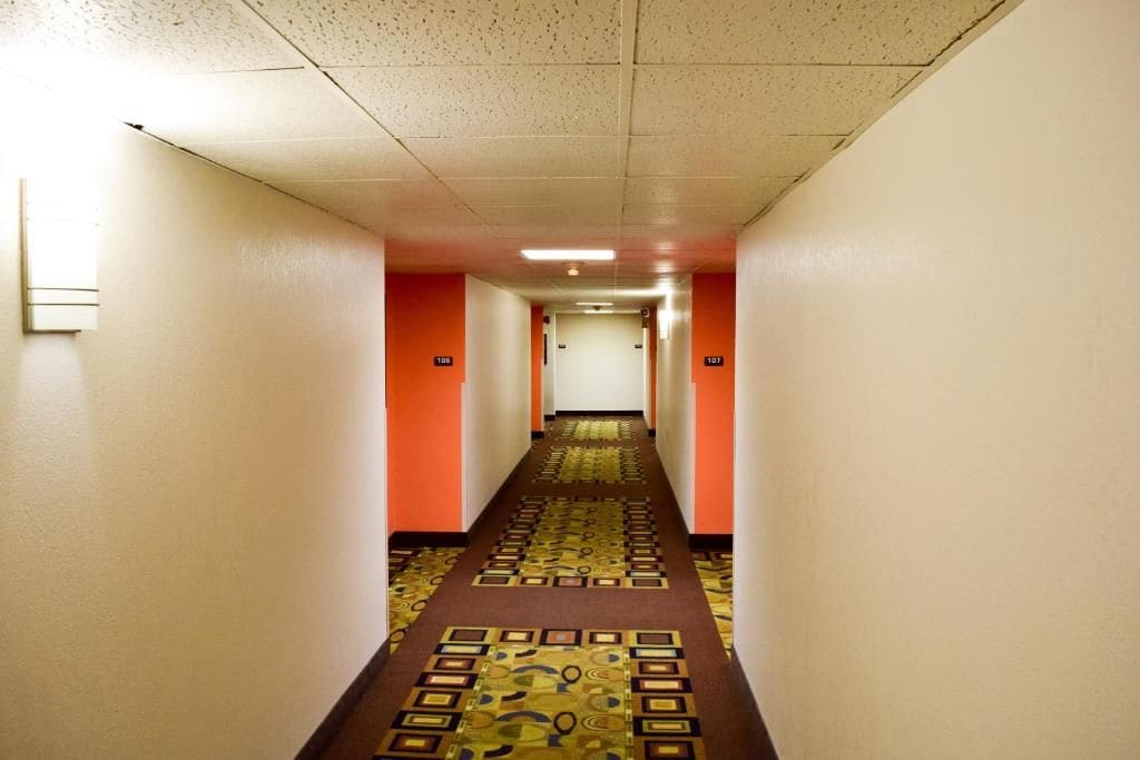 Ein Hotelkorridor mit Teppichböden, weißen Wänden und orangefarbenen Akzenten.