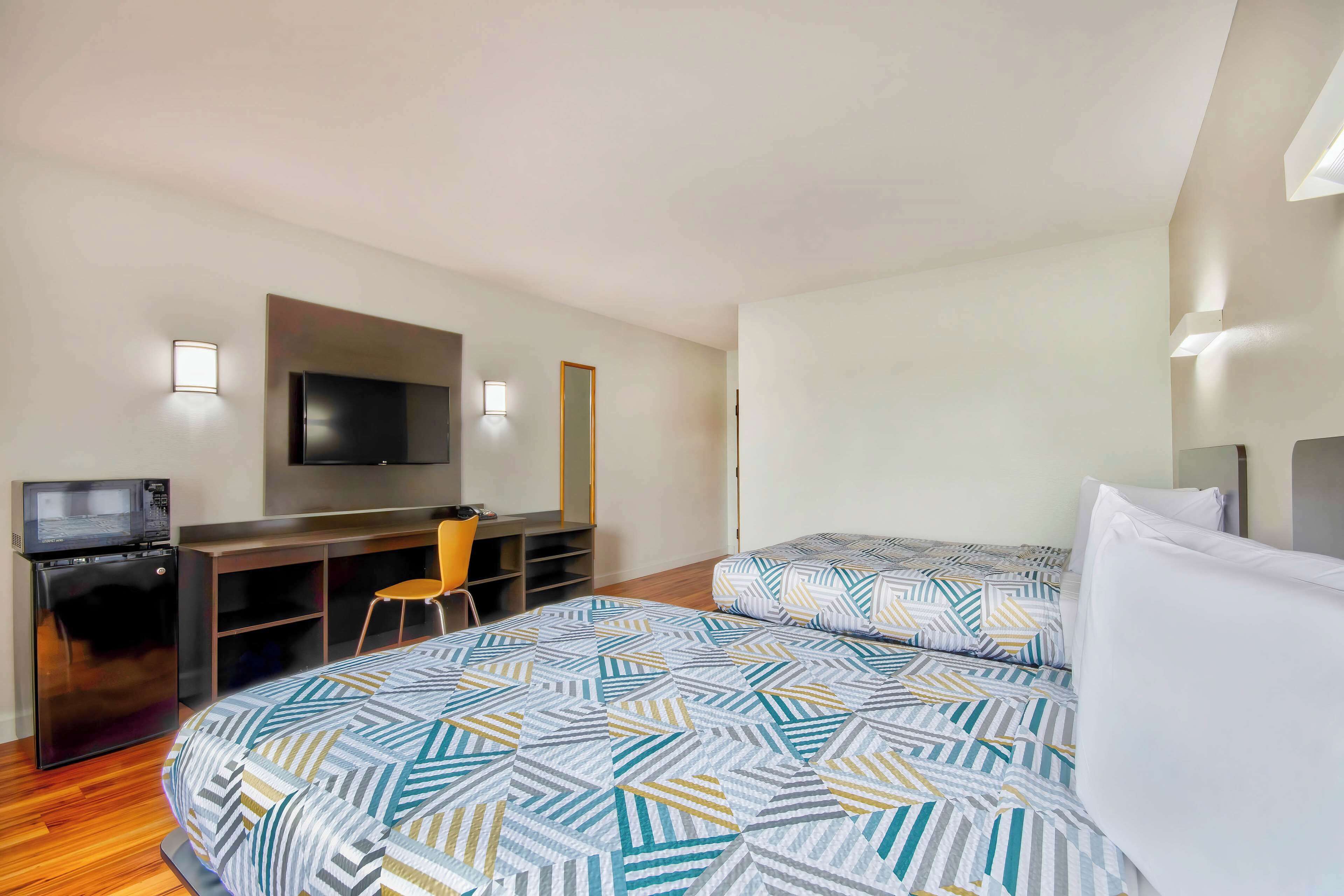 A hotel room with a bed, a desk with a computer, a TV, and a microwave.