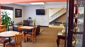 A room with a table and chairs, a television mounted on the wall, and a staircase leading to an upper level.