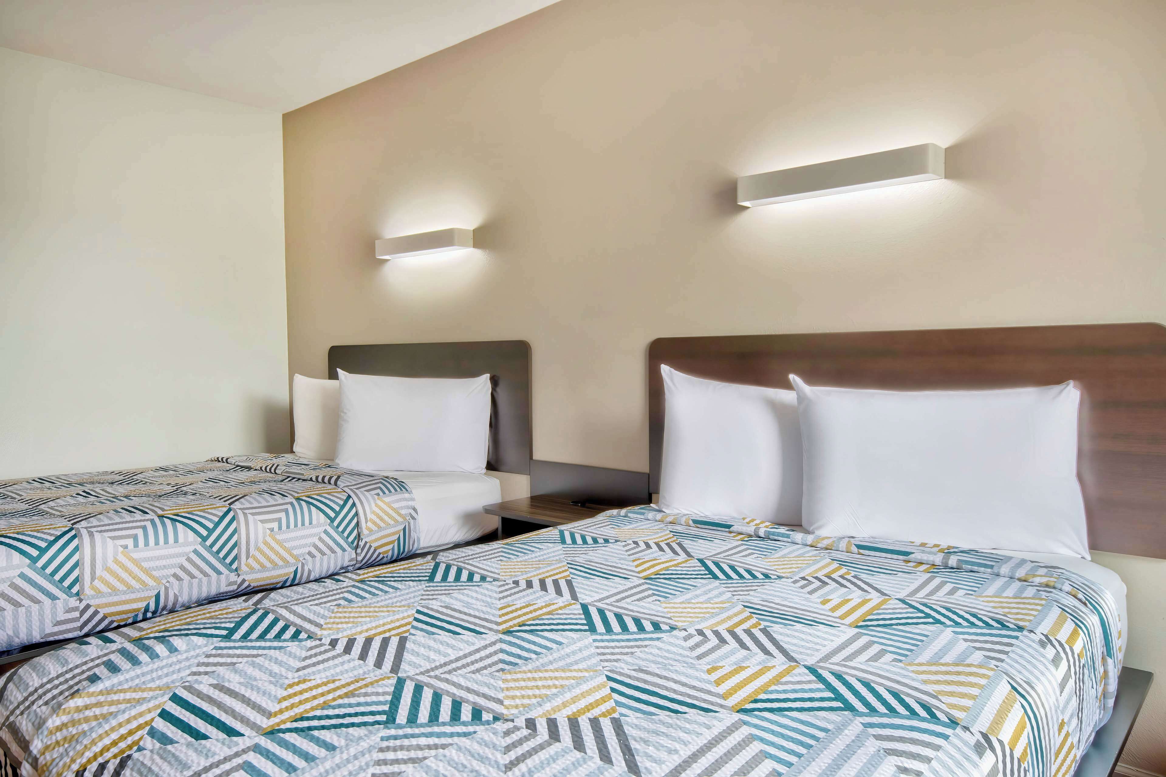 Une chambre d’hôtel avec deux lits, chacun doté d’une literie à motifs, d’une tête de lit en bois et d’un éclairage fixé au mur.