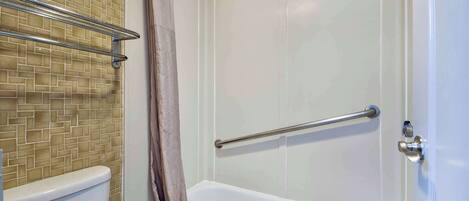 A bathroom with a tiled wall, a bathtub, a toilet, and a shower curtain.
