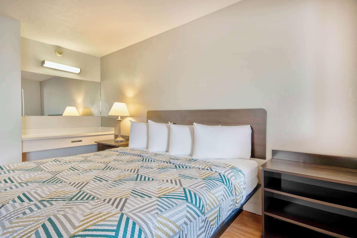 A hotel room with a bed, a nightstand, a mirror, and a wall-mounted shelf.