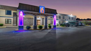 Un motel con un cartel con el número '6', una entrada cubierta y un estacionamiento con vehículos.