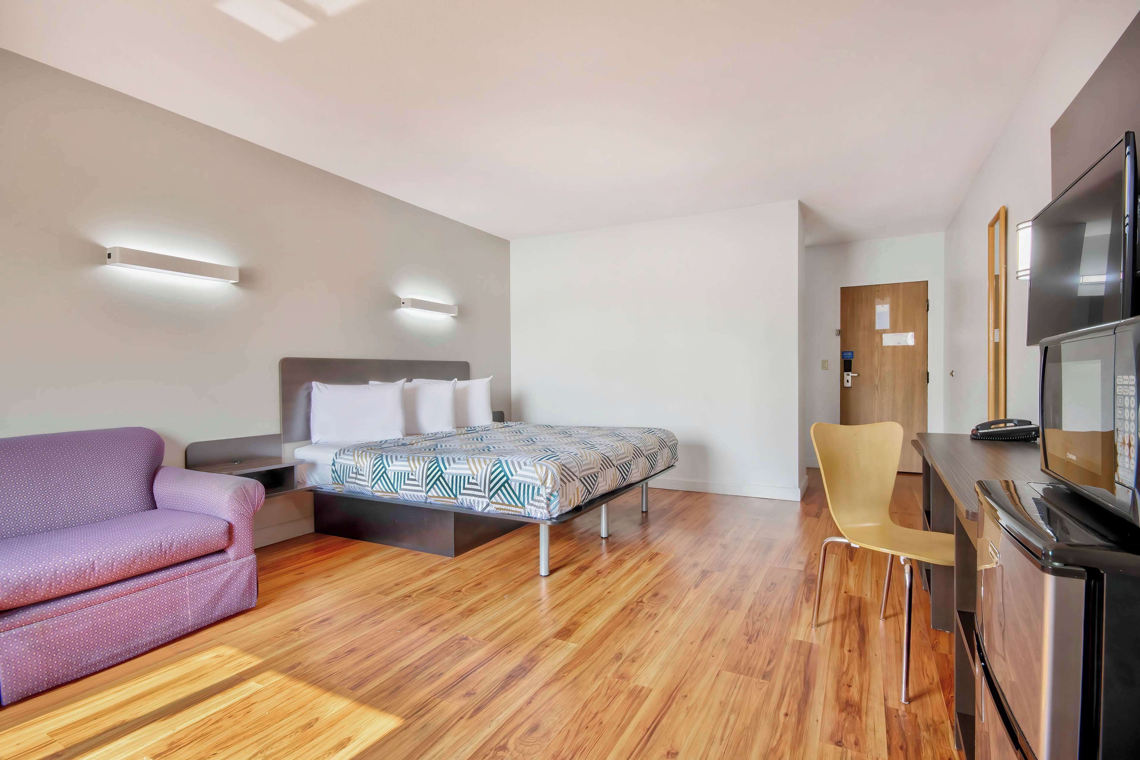 Een moderne hotelkamer met een bed, een slaapbank, een bureau met een televisie en een houten vloer.