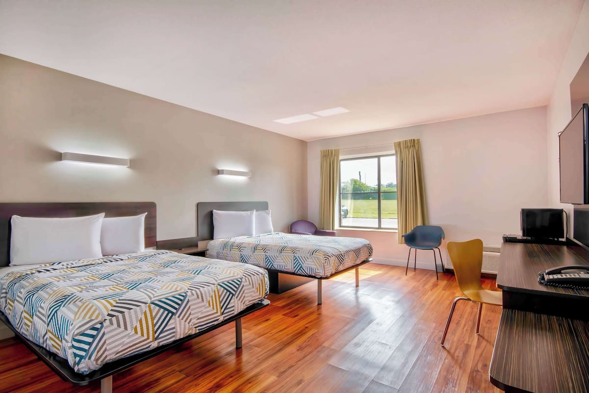 A hotel room with two beds, a desk, a chair, and a TV.