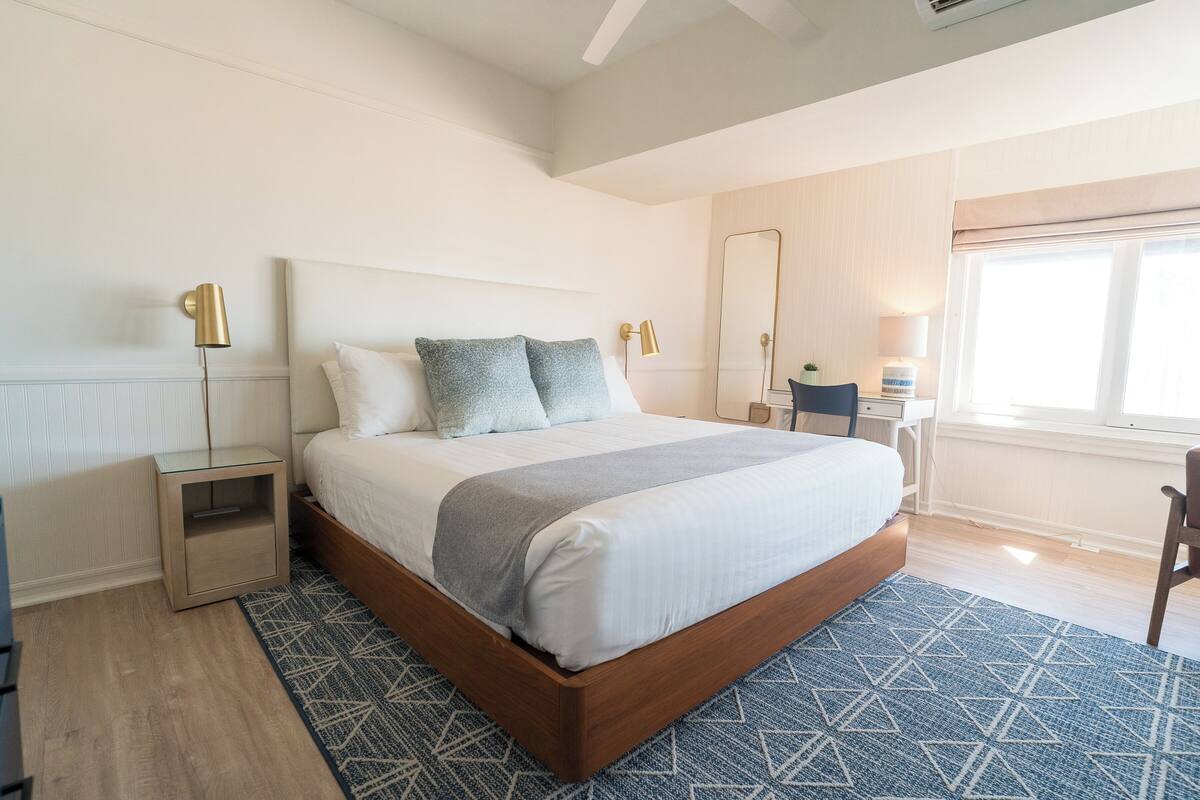 Een moderne slaapkamer met een groot bed, nachtlampen, een spiegel en een raam.
