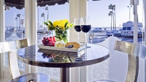 A round table with a glass top, a plate of fruits, a vase of flowers, and two wine glasses.