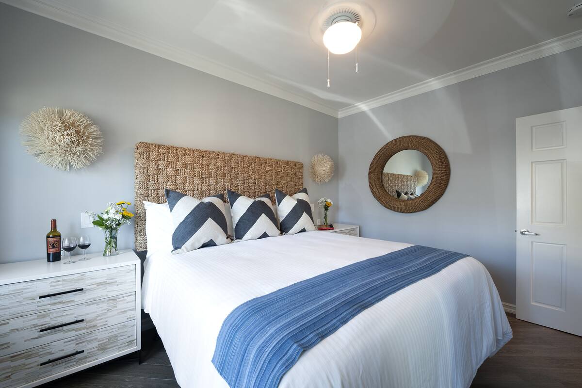 Een keurig opgemaakt slaapkamer met een bed, nachtkastje en een spiegel aan de muur.
