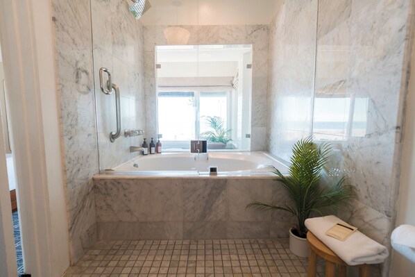 Un baño moderno con piso de mármol, una bañera grande, un espejo, un perchero para toallas y una planta en maceta.