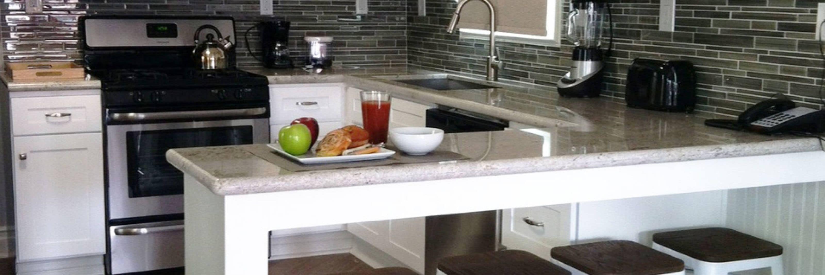 Una cucina con forno, piano cottura e una penisola colazione con un piatto di cibo, un bicchiere di succo e un bollitore.