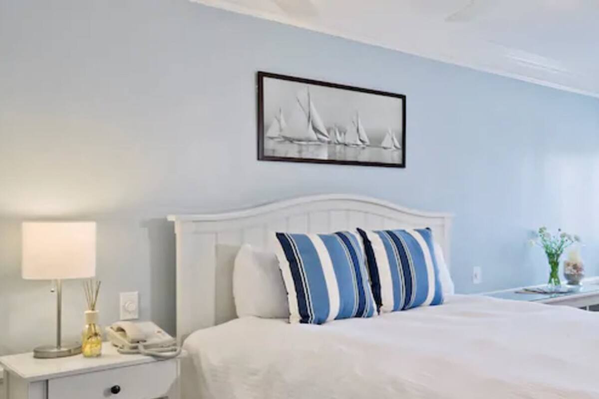 Een netjes ingerichte hotelkamer met een bed, nachtkastje met lamp, telefoon en een lijst aan de muur.