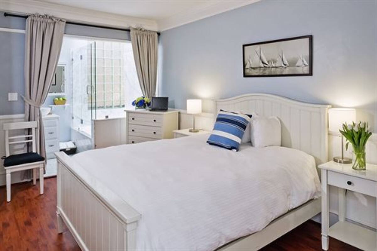 Een keurig opgemaakt slaapkamer met een bed, nachtkastjes, een stoel en een raam met gordijnen.