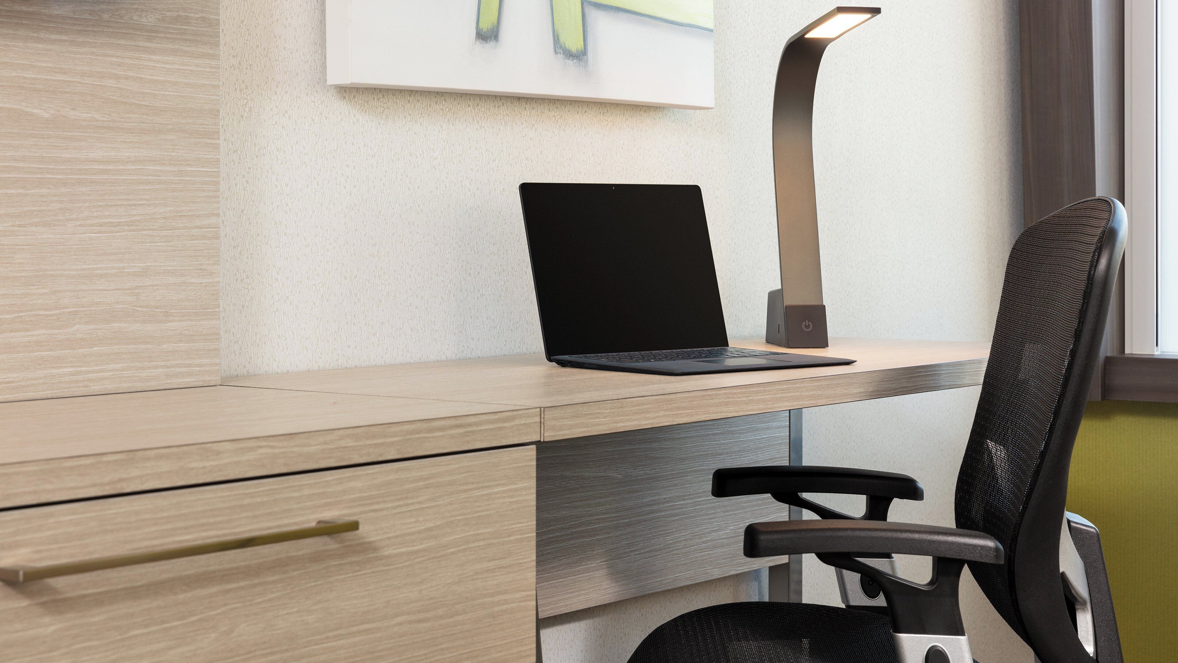 Un escritorio moderno con una computadora portátil, una silla y una lámpara de escritorio.