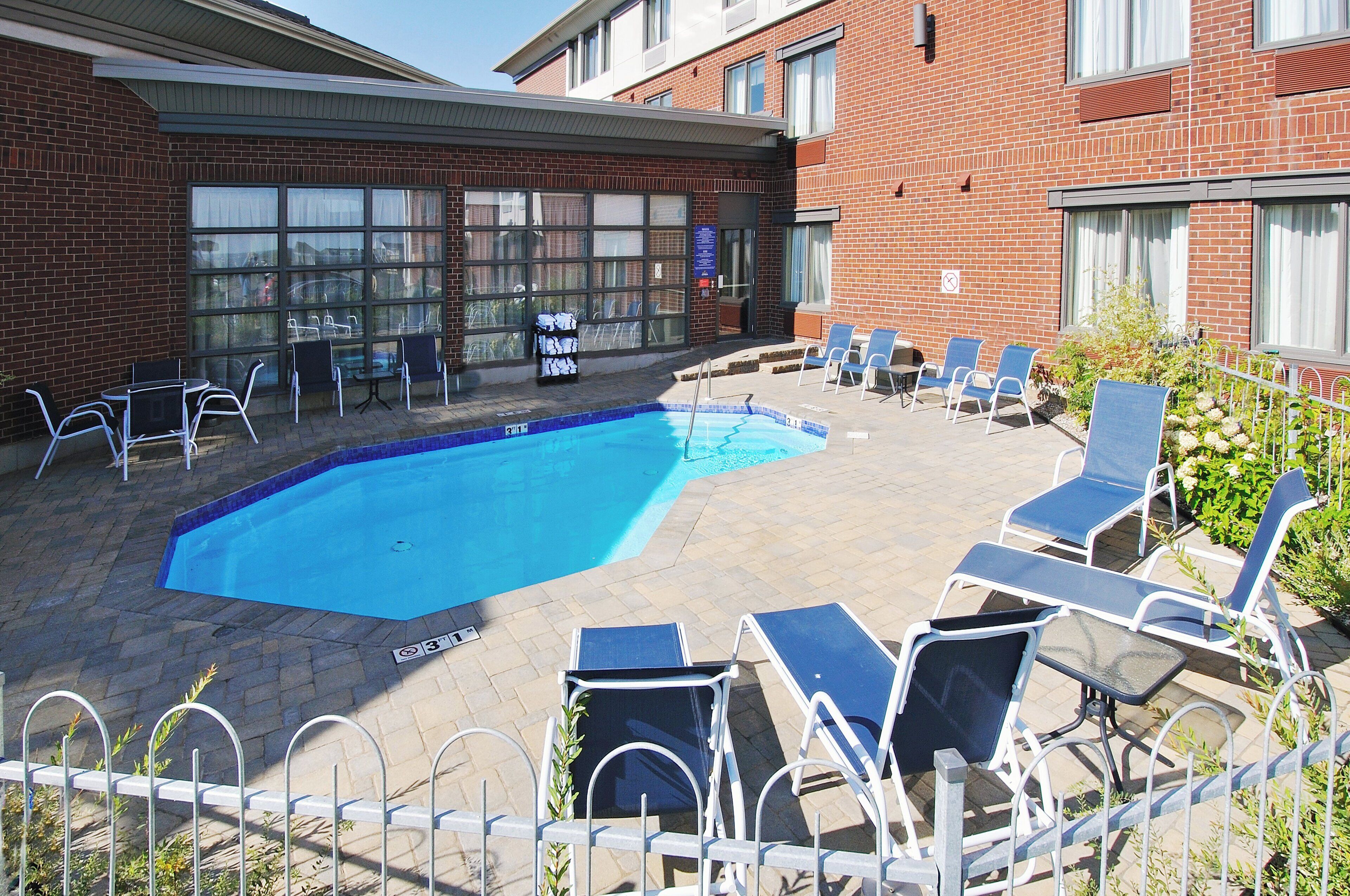A swimming pool with lounge chairs and a brick building in the background.