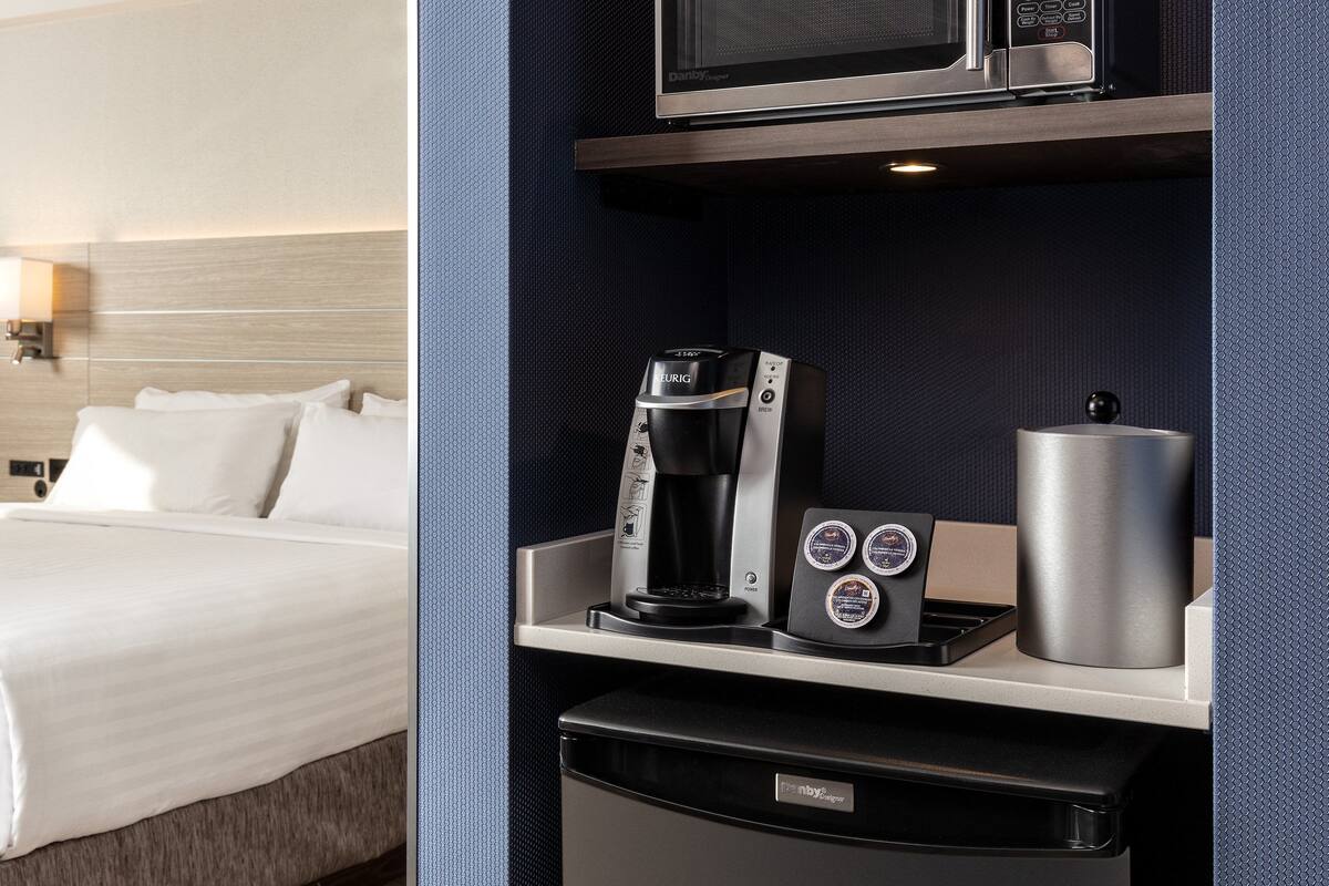 A hotel room with a bed, a minibar, a coffee maker, and a microwave.