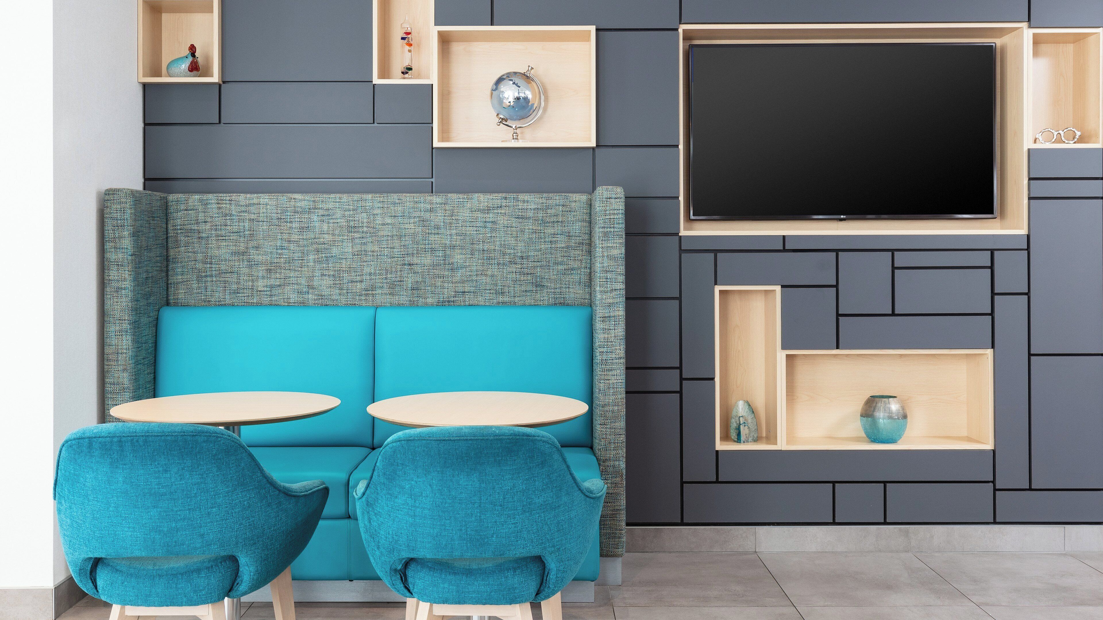 Un salon moderne avec un canapé de couleur turquoise, deux fauteuils assortis, un téléviseur à écran plat et des étagères intégrées ornées d’objets décoratifs.