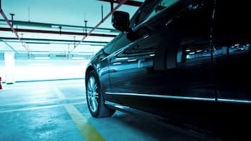 A car parked in a multi-level parking garage with visible structural beams and a yellow line marking the parking spaces.