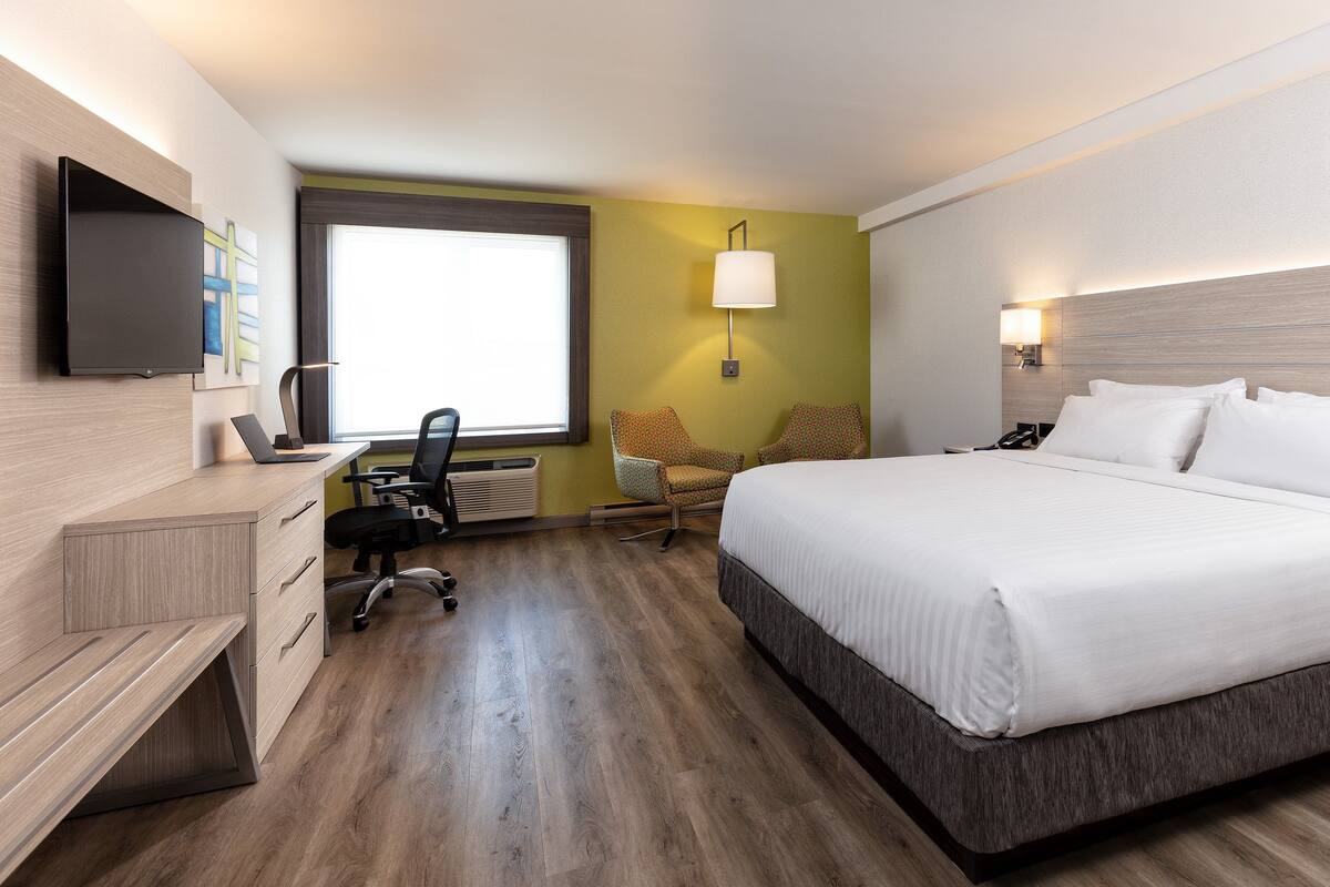 A hotel room with a bed, desk, chair, and a TV on the wall.