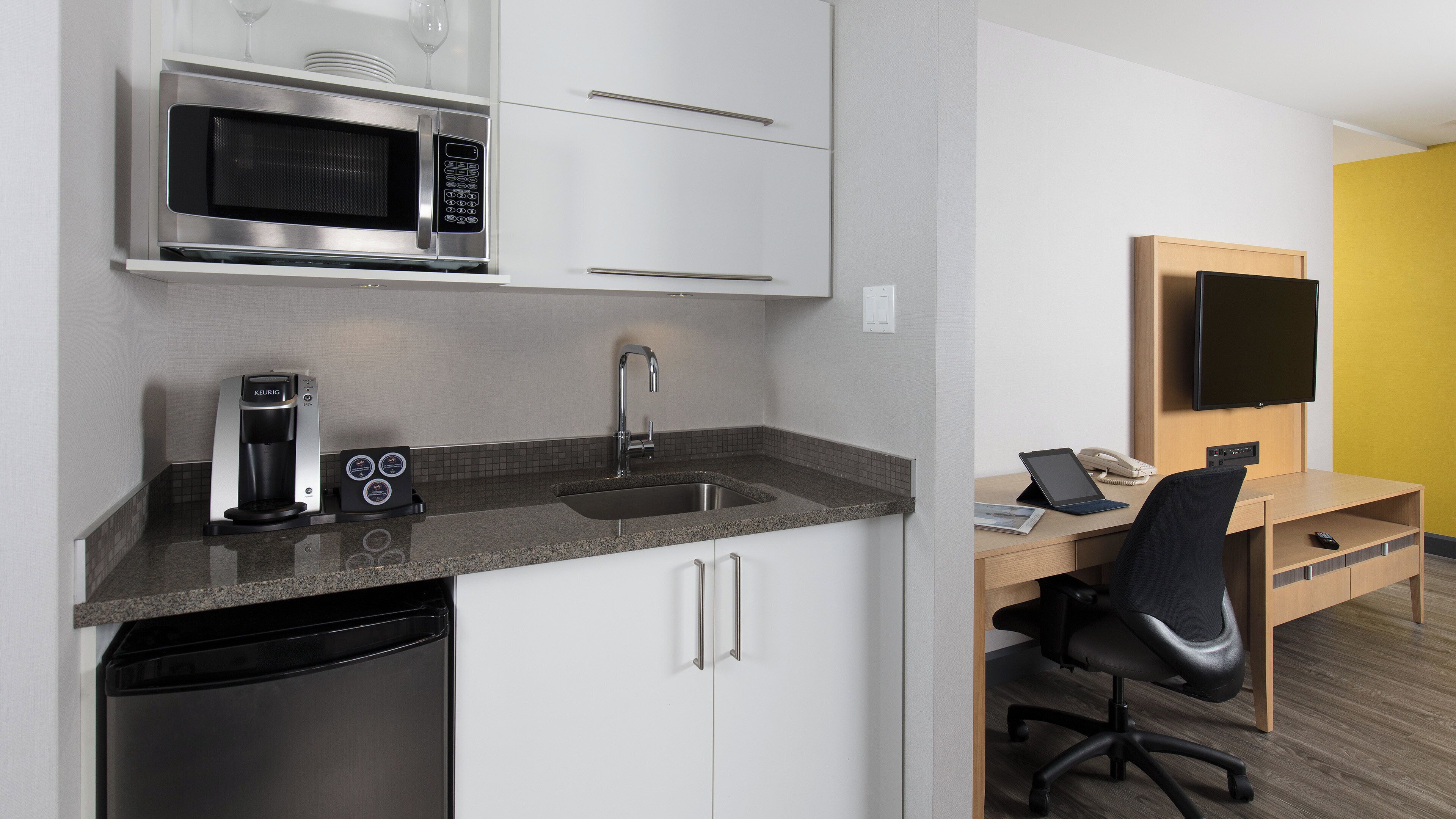 A compact kitchenette with a microwave, coffee maker, and sink.
