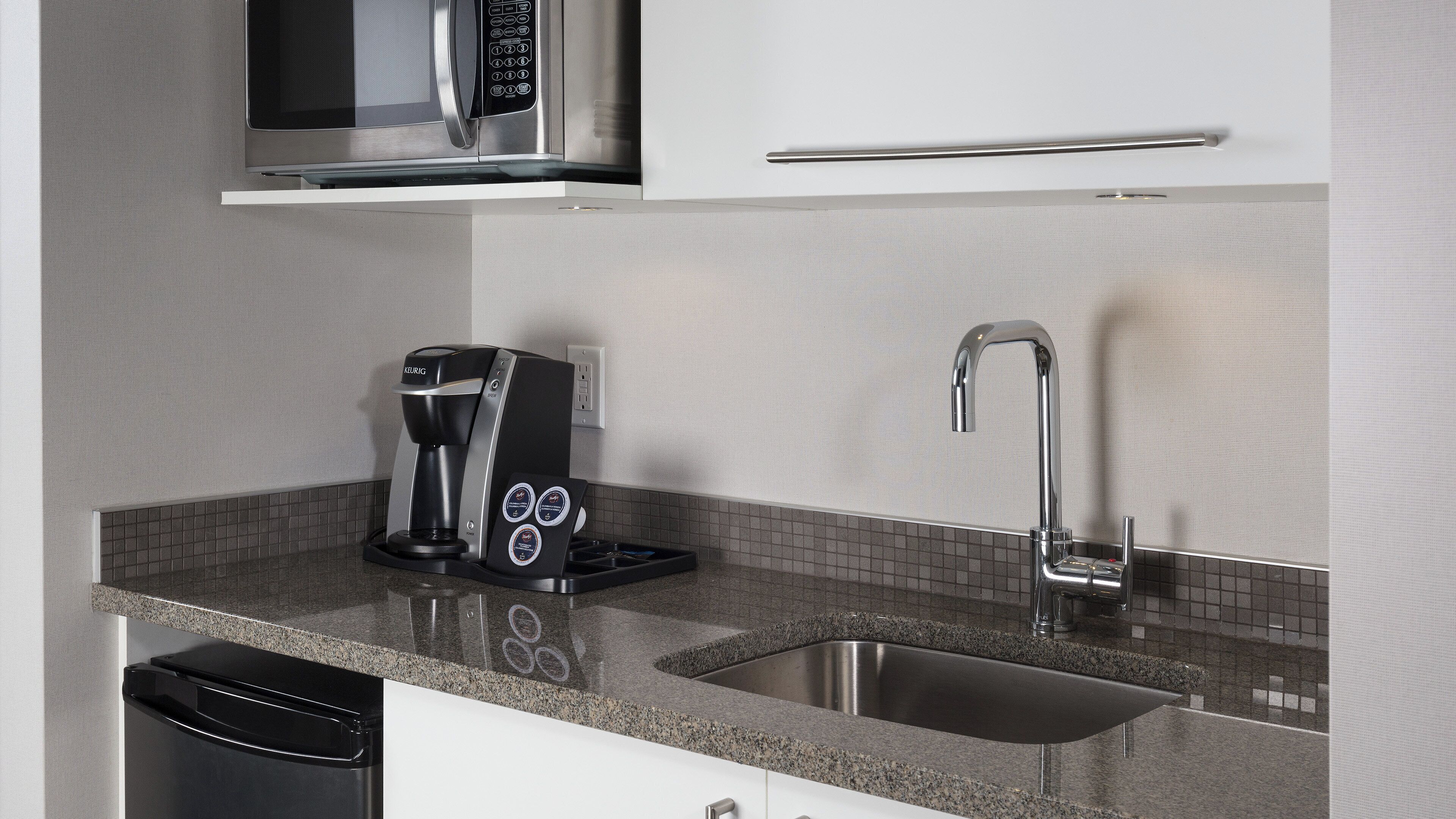 A kitchen with a coffee maker, a microwave, and a stainless steel sink.