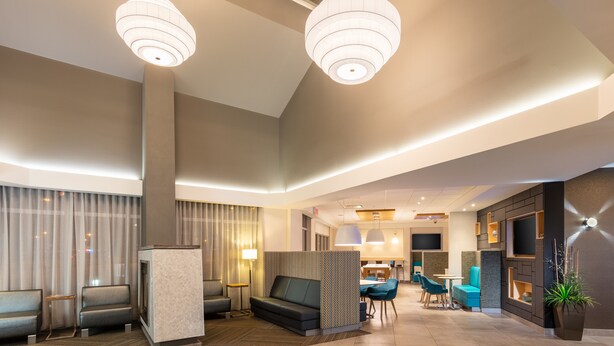 A modern hotel lobby with seating areas, a reception desk, and a TV screen.