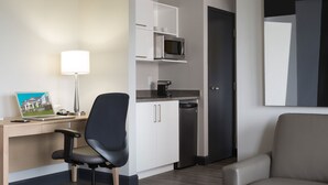 A hotel room with a desk, chair, microwave, coffee maker, and a door.