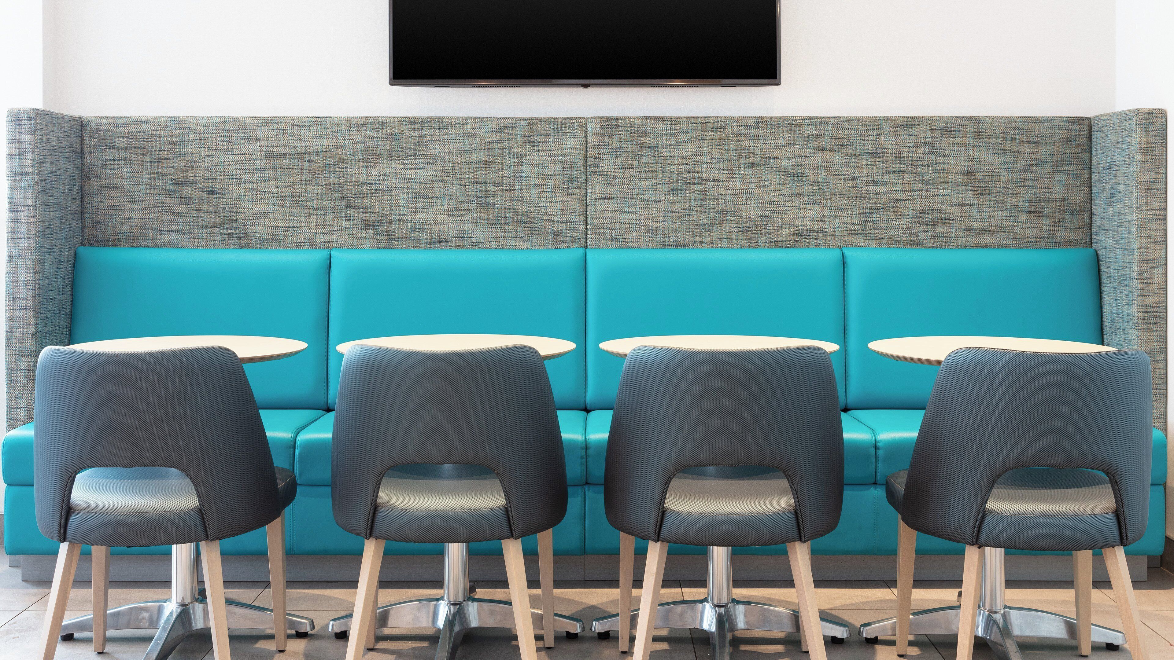 A teal-colored sofa with a textured backrest, four black chairs with metal legs, and two small round tables.