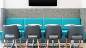 A teal-colored sofa with a textured backrest, four black chairs with metal legs, and two small round tables.