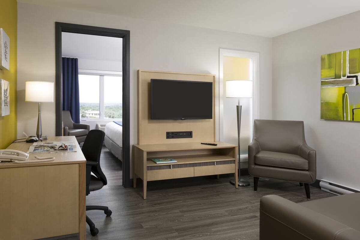 A hotel room with a desk, chair, TV, and a large window.