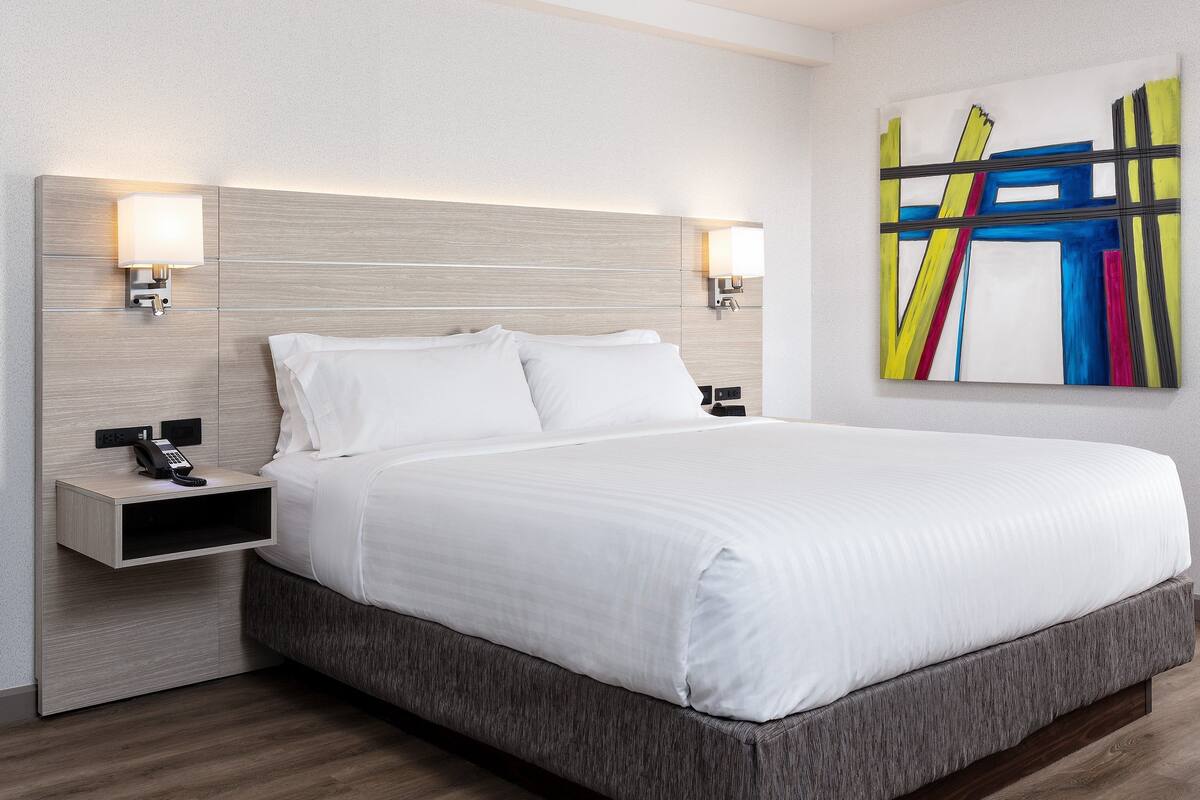A hotel room with a bed, bedside tables, a phone, and a colorful abstract painting on the wall.