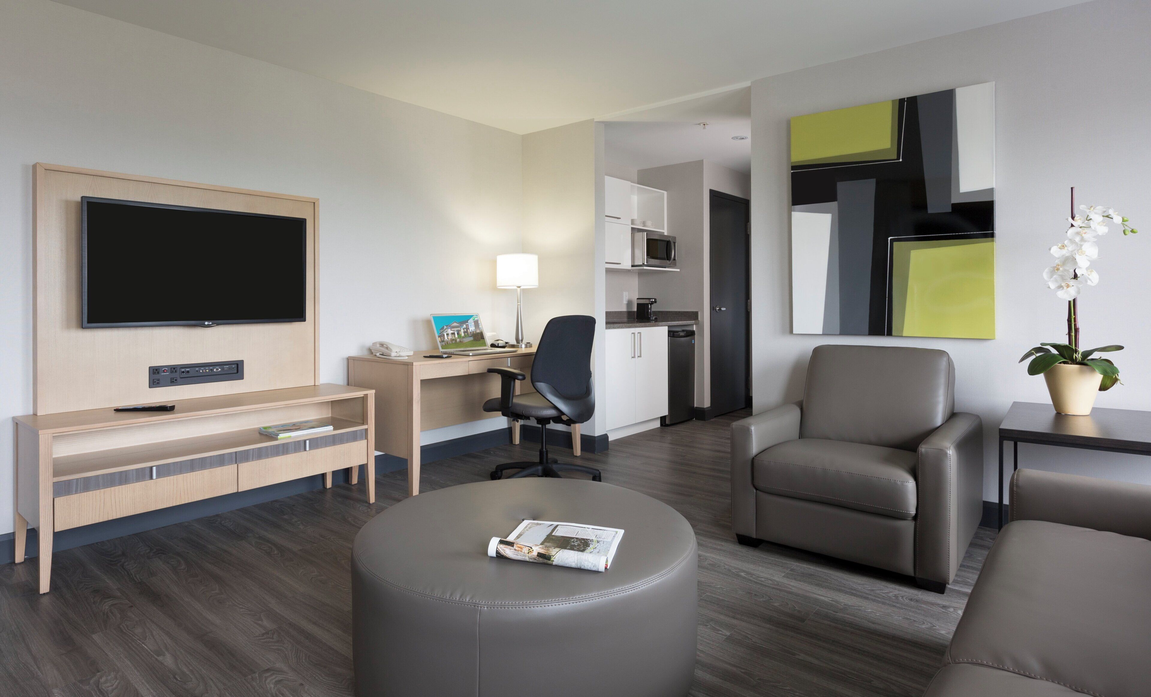 Quarto de hotel com televisão de tela plana, escrivaninha com luminária, cadeira, sofá e mesa pequena com planta em vaso.