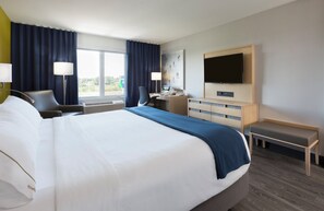 Une chambre d’hôtel avec un grand lit, un bureau, une chaise, une télévision et une fenêtre avec des rideaux.