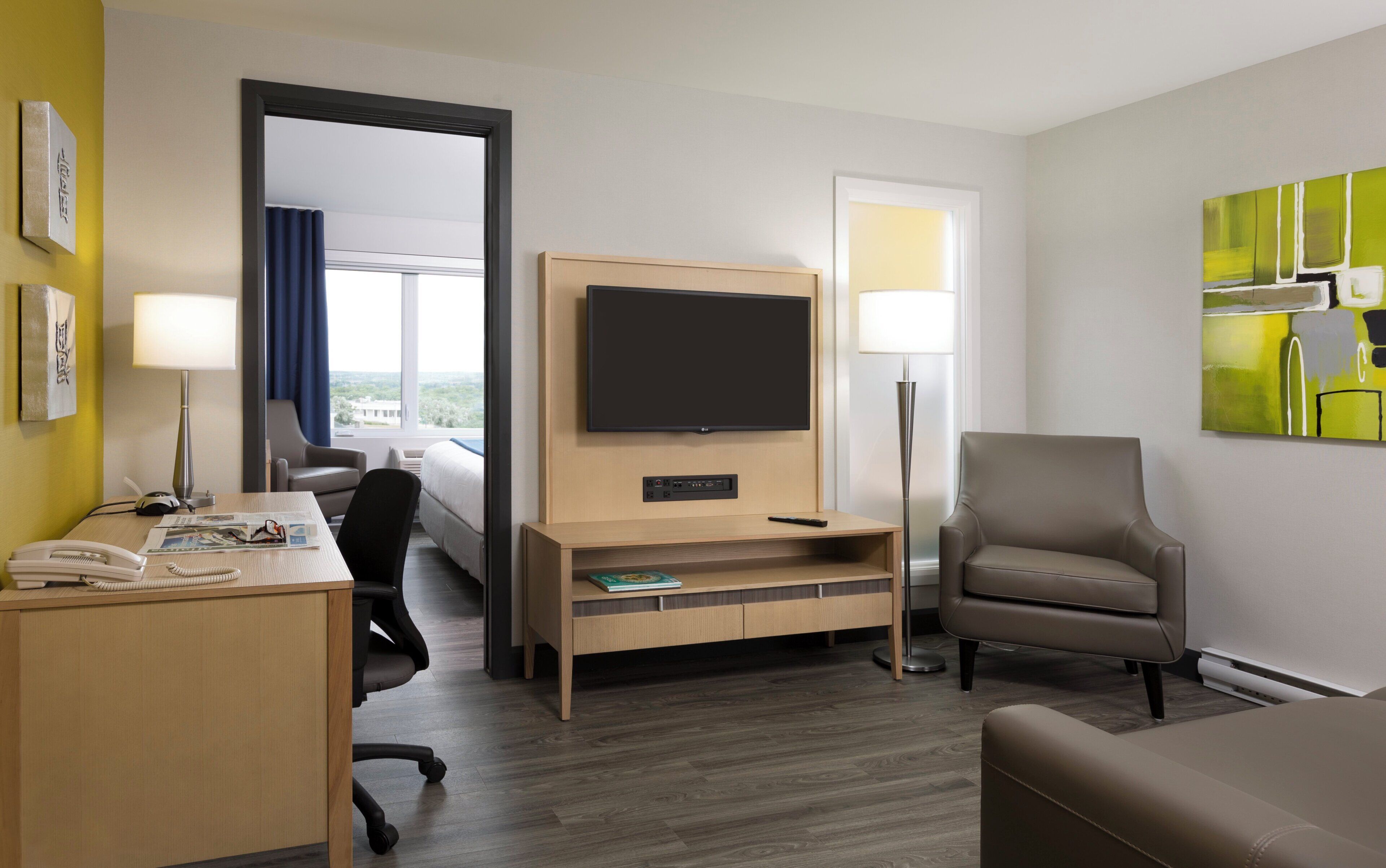 A hotel room with a bed, a desk with a telephone, a chair, a TV, and a lamp.