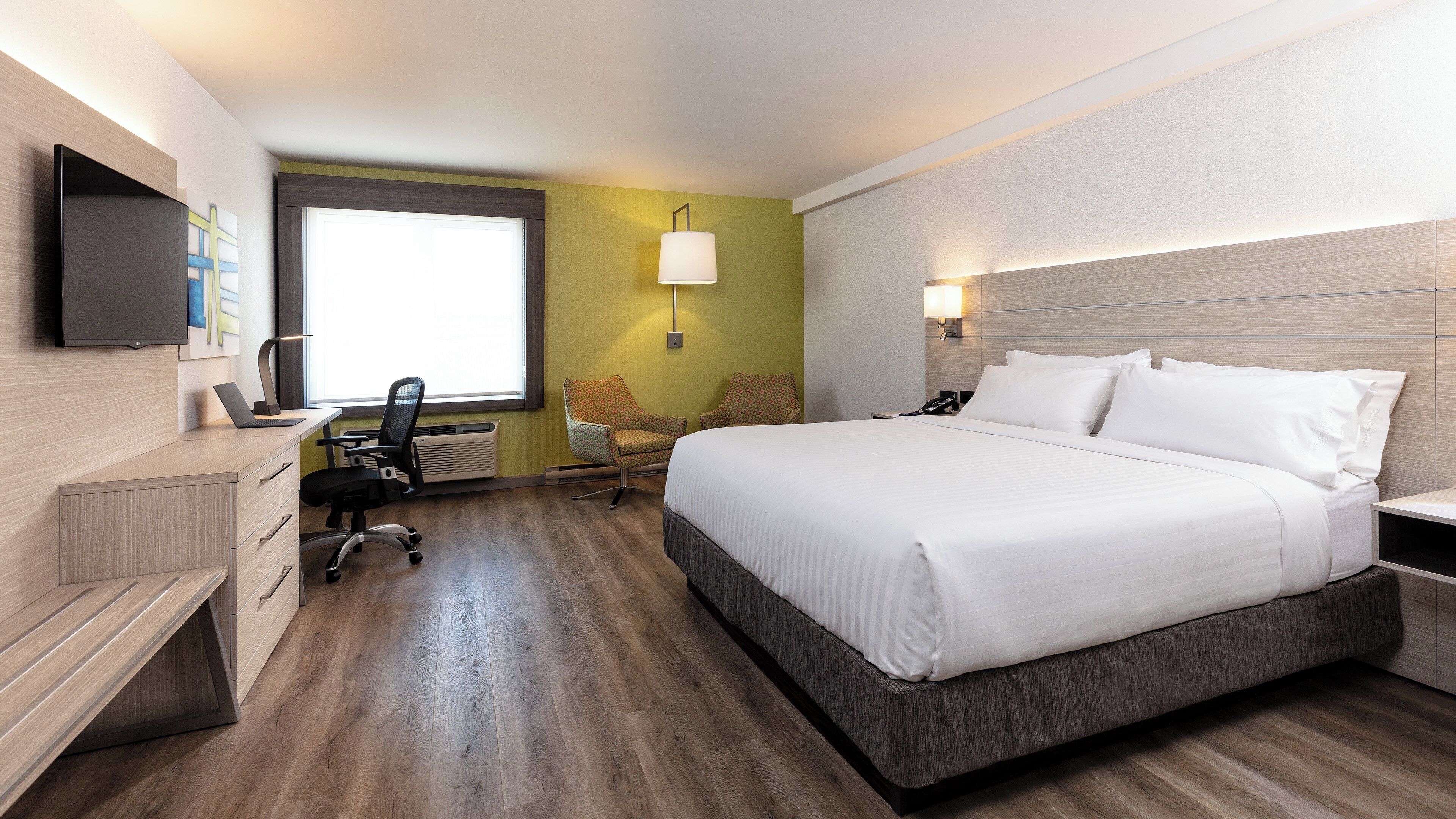 A hotel room with a bed, desk, chair, and a television.