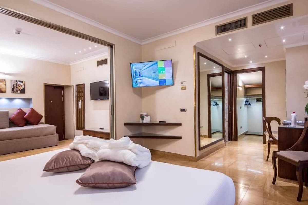 Una camera d'albergo con un letto, una TV a muro, una scrivania e una sedia.