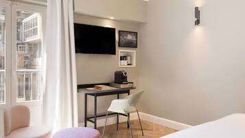 A hotel room with a bed, a desk, a chair, a television, and a window with curtains.