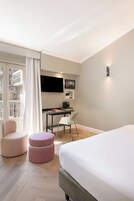 Een hotelkamer met een bed, een bureau, een stoel, een televisietoestel en een raam met gordijnen.