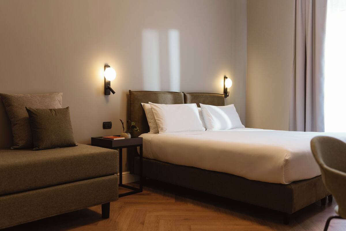 Quarto de hotel com cama, sofá, mesa de cabeceira e uma cadeira.