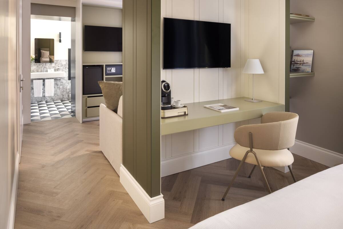 Quarto de hotel moderno com escrivaninha, cadeira, TV de tela plana e máquina de café pequena.