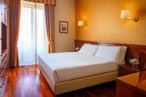 Una camera d'hotel con un letto grande, pavimento in legno, due comodini, un tavolino e un quadro incorniciato appeso al muro.