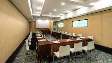 Une salle de conférence avec de longues tables, des chaises blanches et un écran de projection.